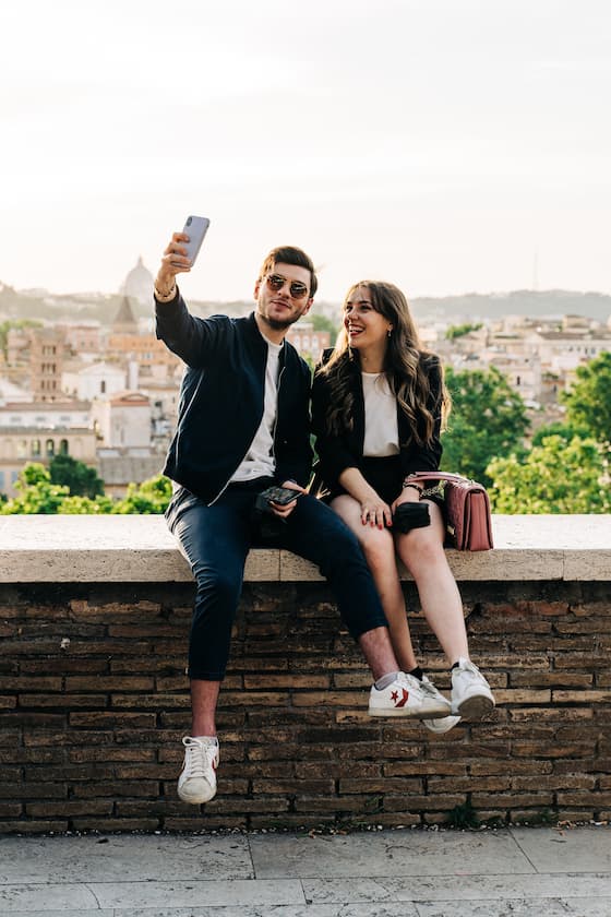 HomeExchange-Video-Challenge: Ehepaar, das in Rom auf einer Mauer sitzt und sich mit einem Handy filmt